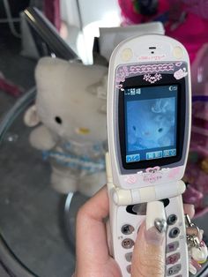 a person holding a cell phone in their hand with a teddy bear on the table behind them