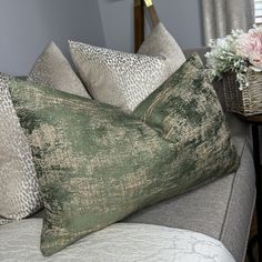 a close up of pillows on a couch near a basket with flowers and a lamp