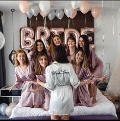 a group of women in pink robes standing on top of a bed next to balloons