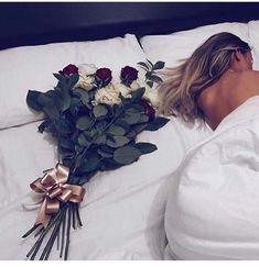 a woman laying in bed next to a bouquet of roses