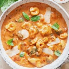 a white bowl filled with pasta and meat soup next to a plate of spinach