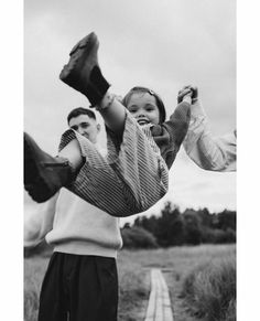 a woman holding a child in the air while standing next to a man on a dirt road