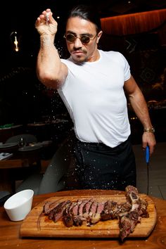 a man standing next to a cutting board with meat on it