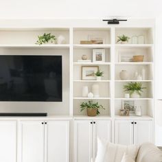 a flat screen tv sitting on top of a white book shelf next to a couch