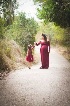 a woman in a red dress is holding her daughter's hand while walking down the road