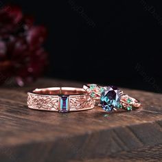 two rings with blue and green stones on top of a wooden table next to flowers