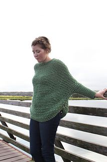 a woman is standing on a bridge by the water wearing a green crocheted sweater