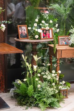 flowers and plants are arranged on small tables in front of a glass wall with pictures