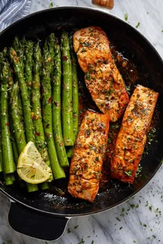 salmon and asparagus in a skillet with lemon wedges