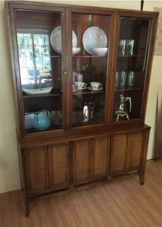 a wooden china cabinet with glass doors and plates on the top, sitting in a living room