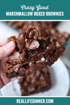 a hand holding a chocolate brownie with marshmallows in the background and text overlay that reads crazy good marshmallow boxed brownies