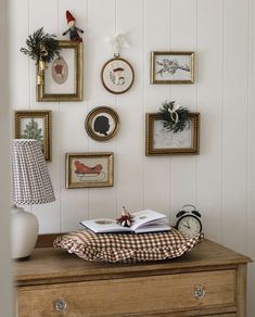 a wooden dresser topped with an open book and lots of framed pictures on the wall