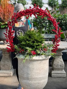 a woman walking past a large potted plant with red berries and greenery in it