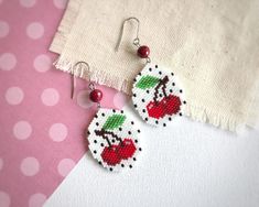 a pair of earrings with cherries on them sitting next to a piece of fabric