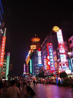 many people are walking around in the city at night with brightly lit buildings and signs