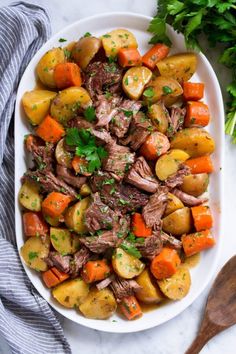 a white plate filled with meat and potatoes on top of a marble table next to parsley