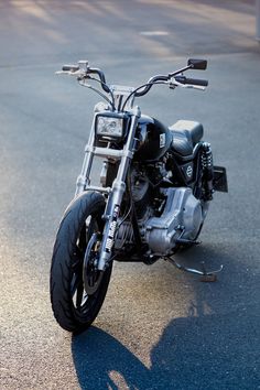 the motorcycle is parked on the side of the road with its shadow cast by it's front wheel