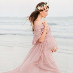 a pregnant woman wearing a flower crown standing on the beach