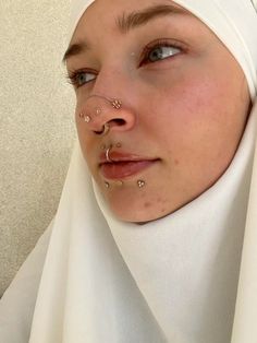 a woman with piercings on her nose wearing a headscarf and white scarf