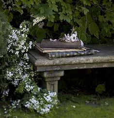 an old book sitting on top of a stone bench in the middle of some flowers