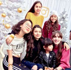 a group of young women sitting next to each other in front of a christmas tree