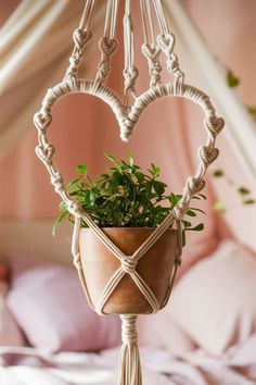 a potted plant hanging from a macrame heart - shaped holder on a bed