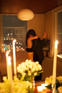 two people embracing each other in front of candles and vases with flowers on them