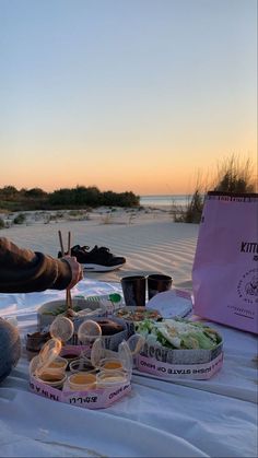 a table topped with lots of food on top of a white cloth covered field next to the ocean