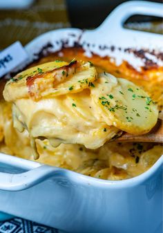 a casserole dish with potatoes and parmesan cheese is being held by a wooden spoon