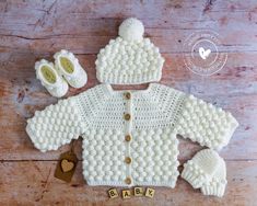 a crocheted baby sweater and booties on a wooden surface with the word baby spelled out