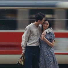 a man and woman standing in front of a train with their arms around each other