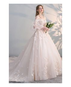 a woman in a wedding dress with flowers on the shoulder and long sleeves, standing against a white wall