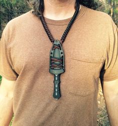 a man wearing a necklace with a large knife pendant on it's neck, in front of some trees