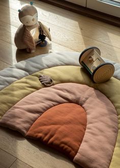 a stuffed animal sitting on top of a wooden floor next to a rug with an orange and pink circle