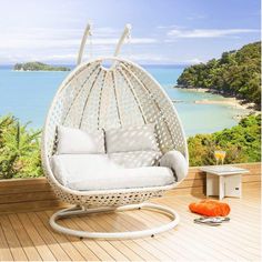 a white wicker swing chair sitting on top of a wooden deck next to the ocean