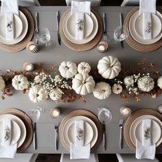 the table is set with white pumpkins and place settings