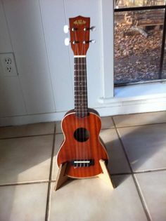 a wooden ukulele sitting on top of a tile floor next to a window