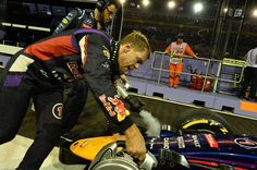 a man is working on a race car in the pit area with other people watching