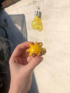 a hand holding a yellow toy giraffe in front of a white brick wall