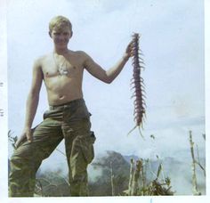 a shirtless man holding a fish in his right hand while standing on the beach