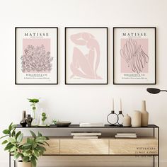 three framed art prints hang on the wall above a table with vases and plants