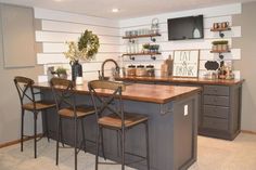 a kitchen island with four chairs and a television mounted above it, in front of two bar stools