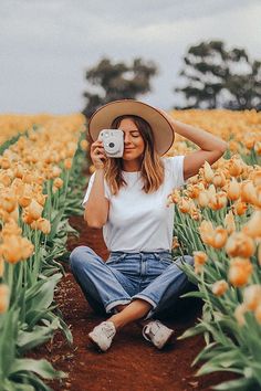 a woman sitting in a field with yellow tulips holding a camera to her face