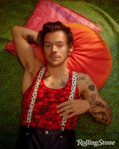 a man laying on top of a bed next to an orange and green pillow with tattoos