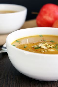 a bowl of soup on a table next to an apple and another bowl of fruit