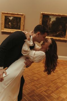 a bride and groom kissing in front of paintings