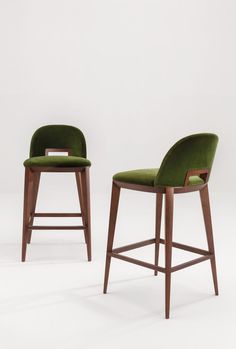 two green chairs sitting side by side in front of a white wall and one has a wooden frame