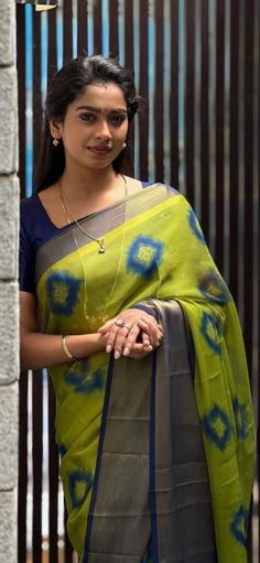 a woman wearing a green and blue sari standing in front of a metal fence