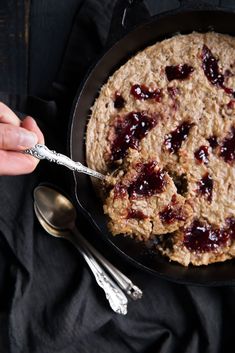 a person holding a spoon in a skillet filled with oatmeal and jelly