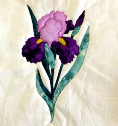 a purple flower with green leaves on a white sheet that has been embroidered onto it